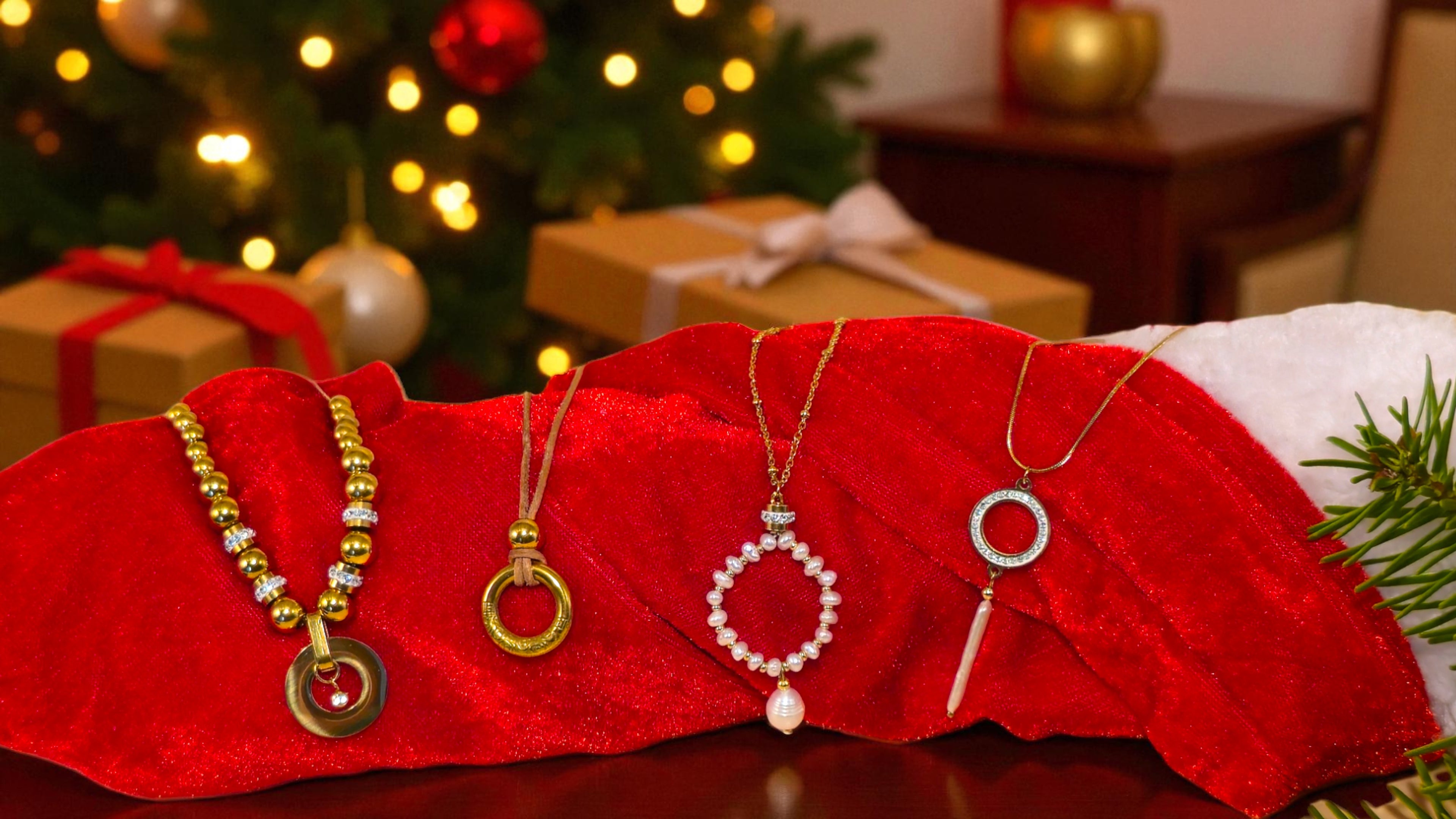 Four necklaces on a red cushion with a Christmas tree and presents in the background